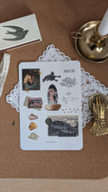 Sticker sheet featuring imagery associated with mermaids, such as shells, the ocean and seaweed. The sheet is sitting on a white doily on a wooden surface.