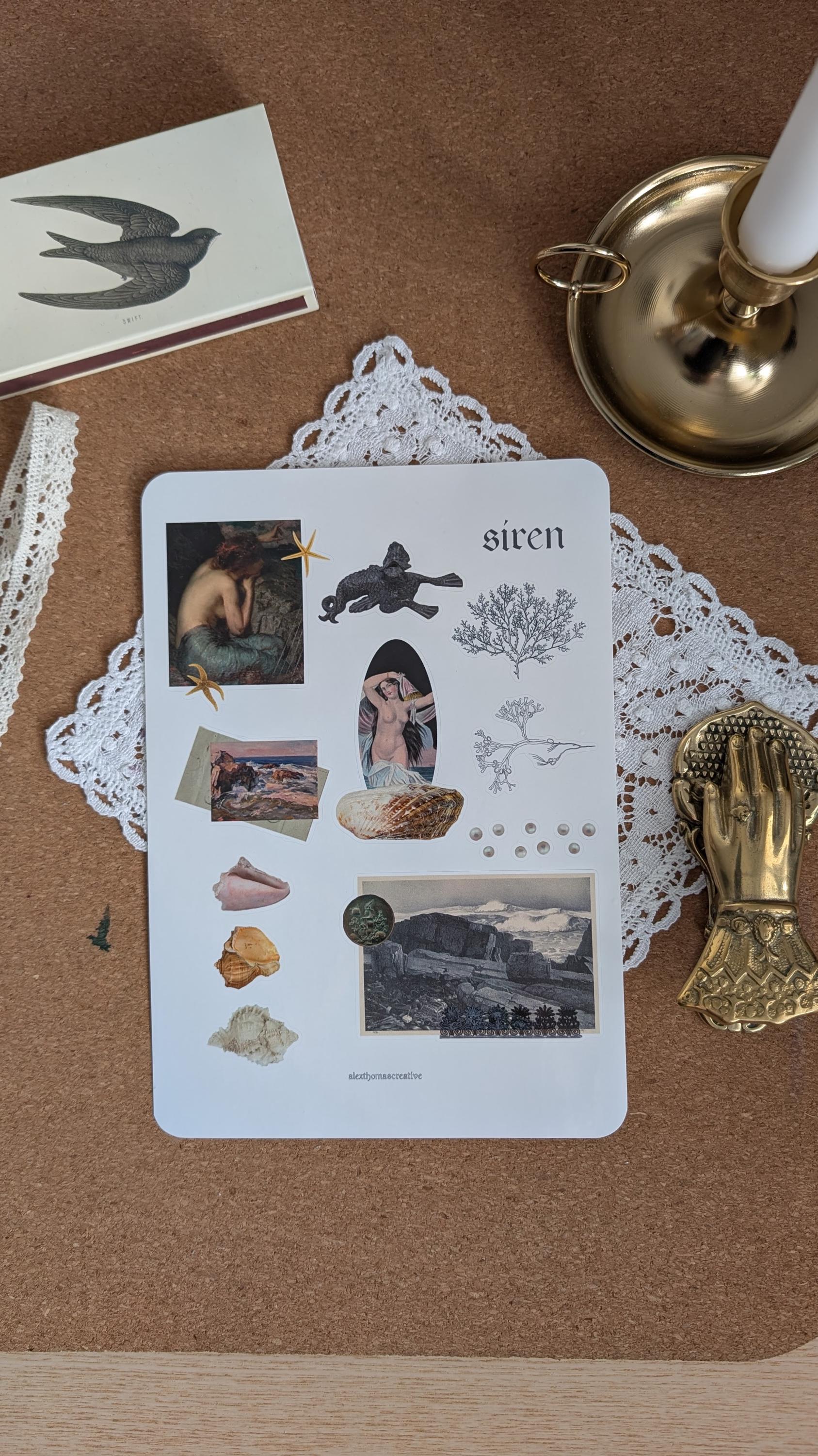 Sticker sheet featuring imagery associated with mermaids, such as shells, the ocean and seaweed. The sheet is sitting on a white doily on a wooden surface.
