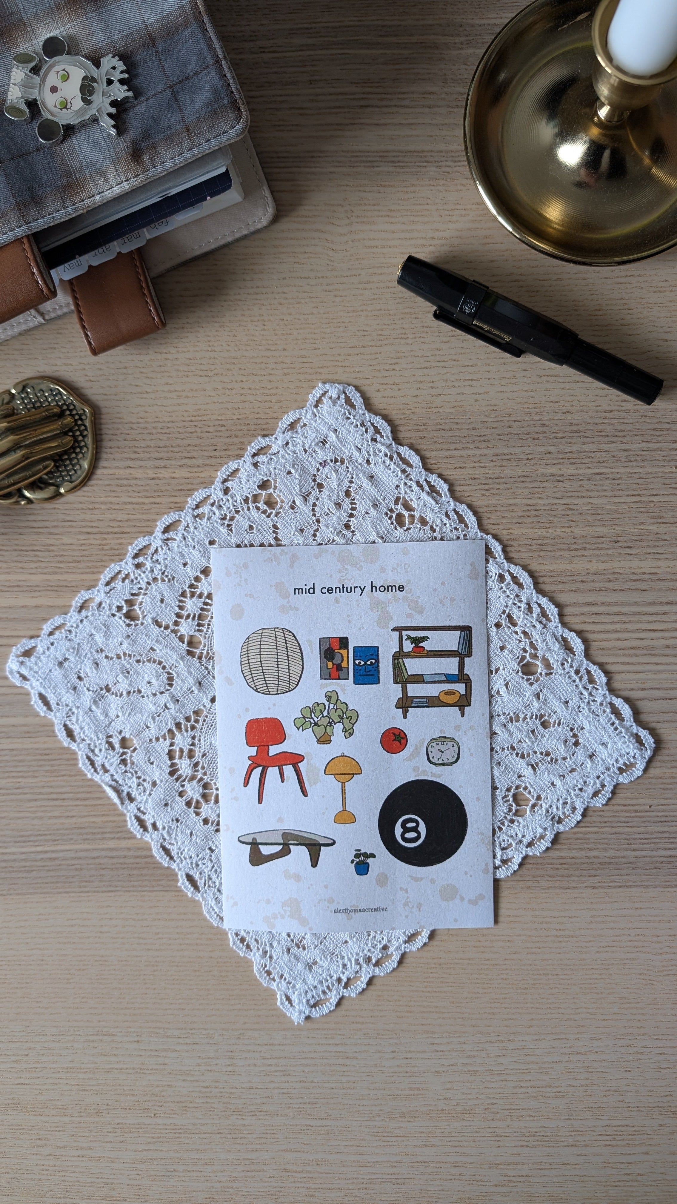Sticker sheet feating illustrations of mid-century furniture. The sticker sheet is sitting on a lace doily on a wooden surface.