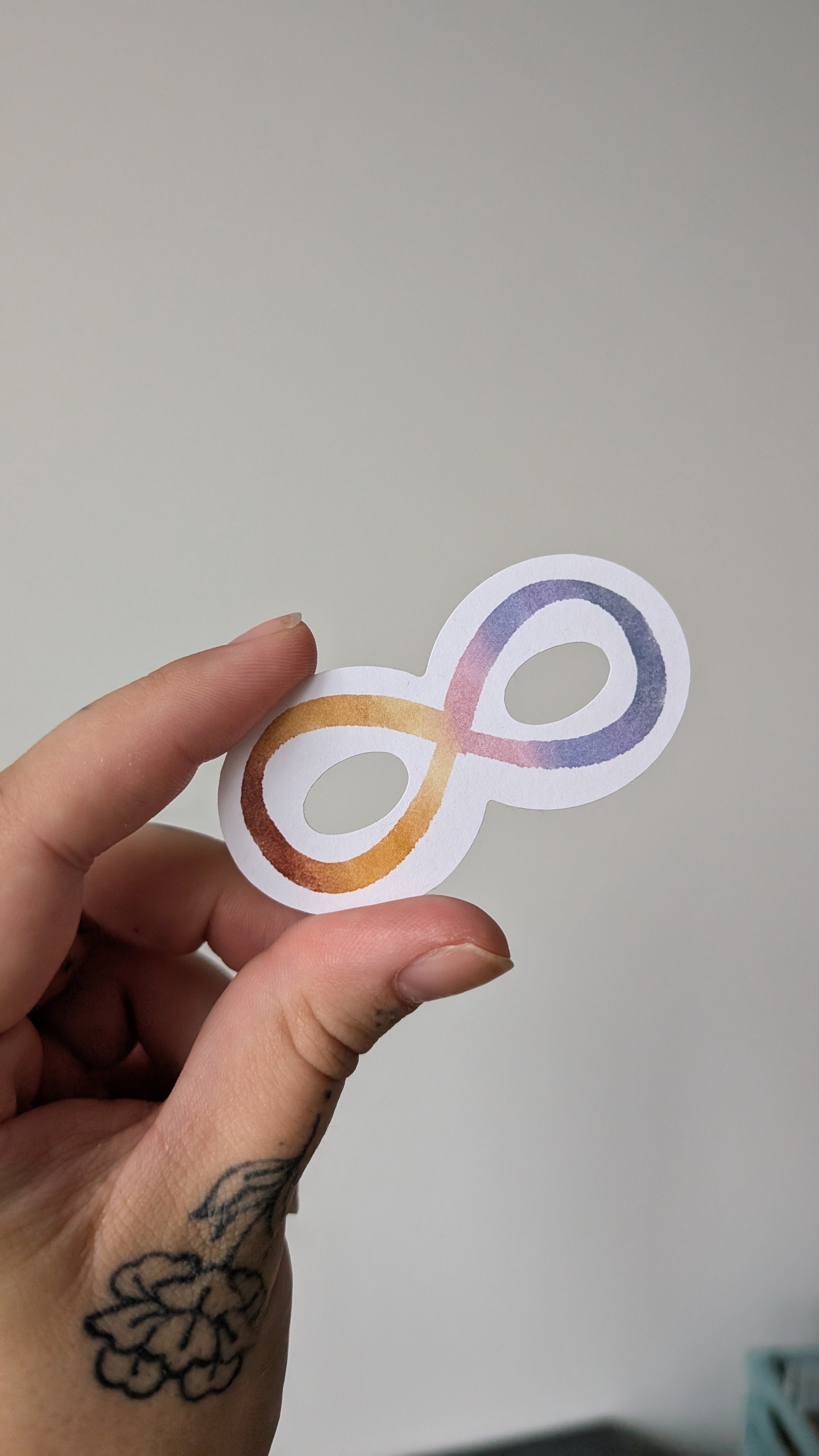 Sticker of an infinity symbol featuring the colours red, yellow, pink and purple (reminiscent of colours seen during a sunset).